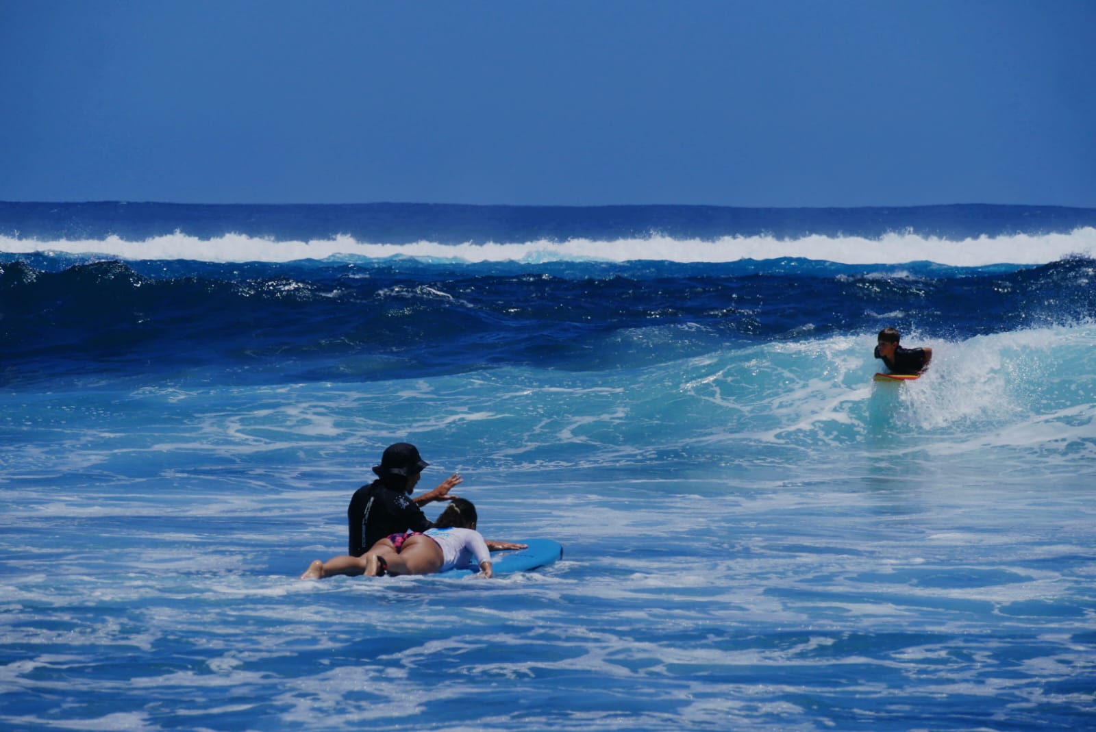Marin accompagne une élève en surf tandis qu’un enfant pratique le bodyboard au Bord d’Étang-Salé